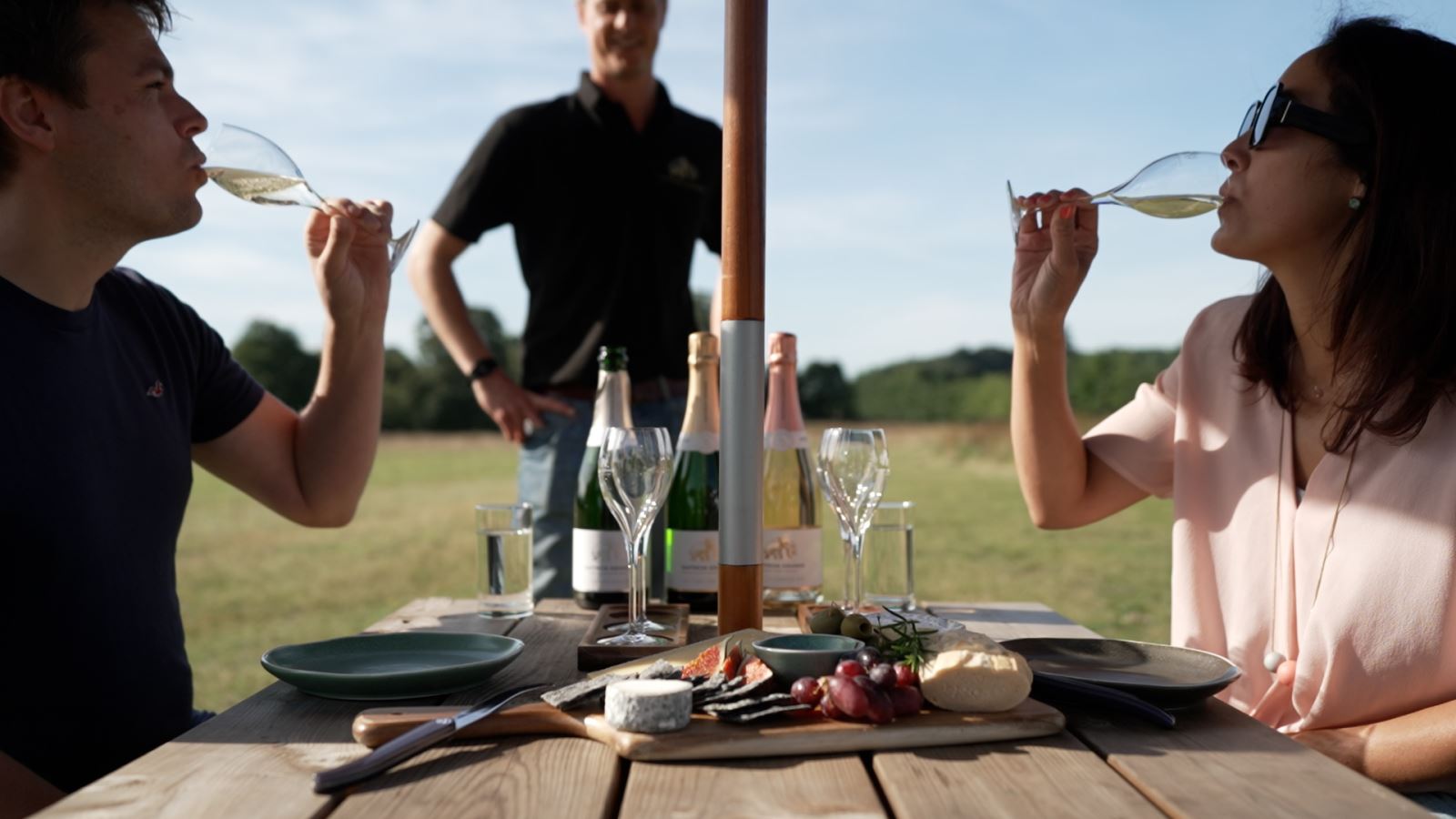 Couple sat outside drinking wine and eating from a food platter at Saffron Grange Vineyard